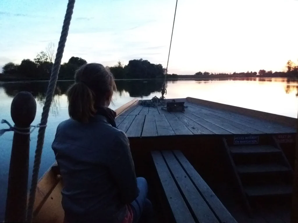 Dame de dos qui admire le coucher du soleil sur un bateau sur la Loire 