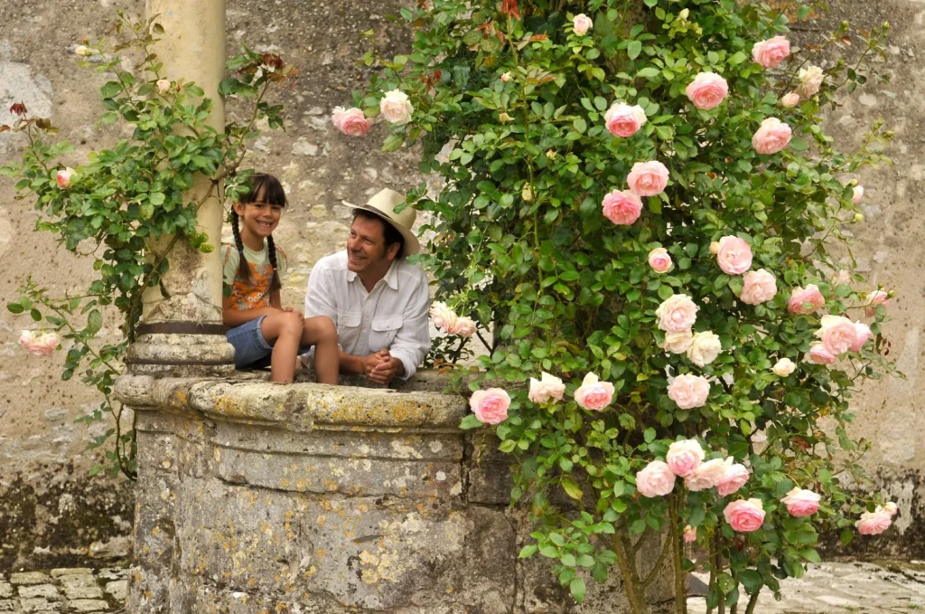 Visiteurs appuyés sur un puits, un rosier grimpant en fleur sur un pilier