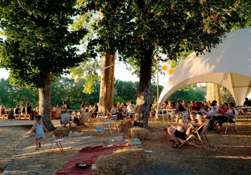 Familles attablées et gens dans des transats sous les arbres, à La Paillote