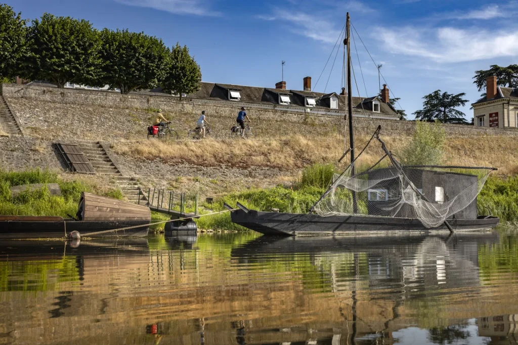 Bateau traditionnel amarré, des cyclistes passent sur un chemin au-dessus