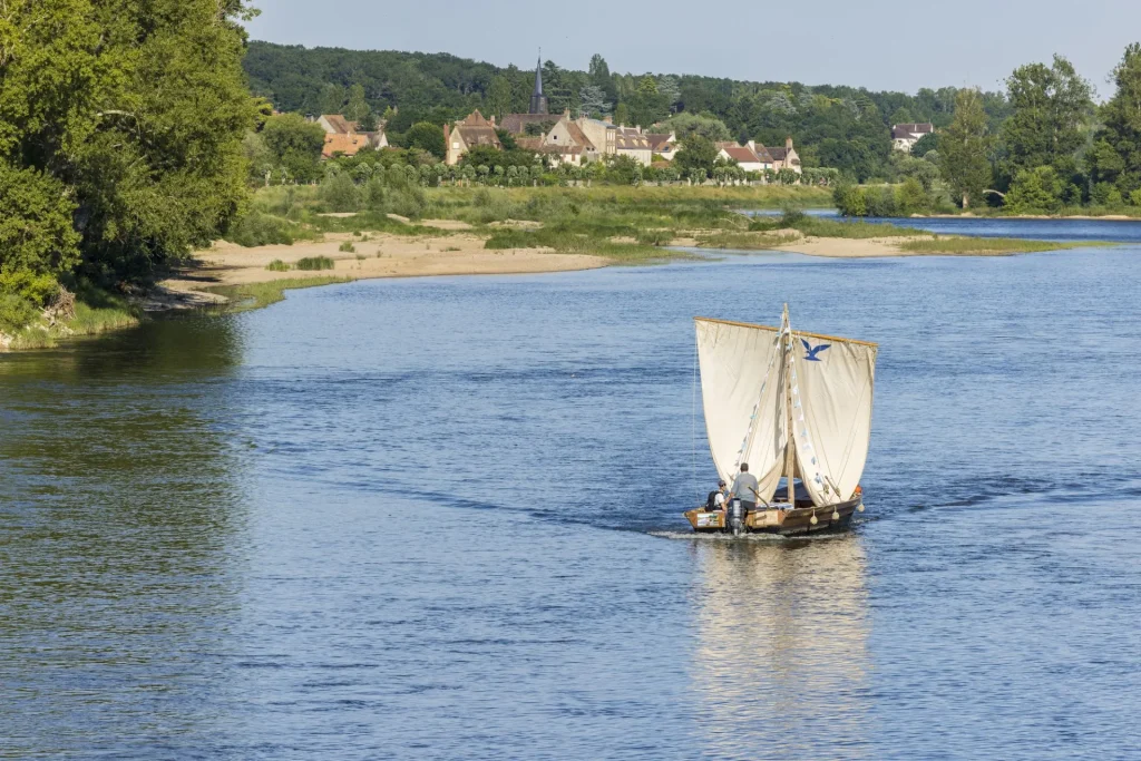 Un bateau naviguant au milieu du fleuve, les voiles sont levées