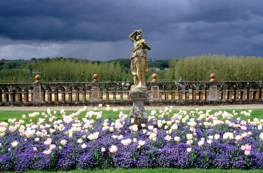 Mélange de fleurs mauves et de tulipes blanches au pied d'une statue