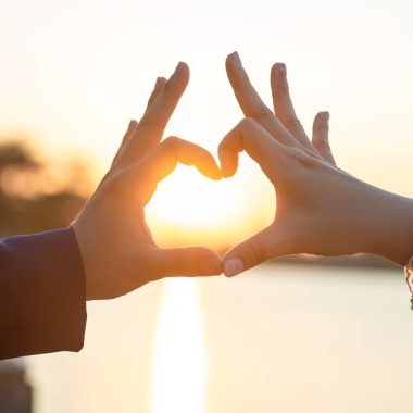 Mains formant un cœur devant le soleil couchant